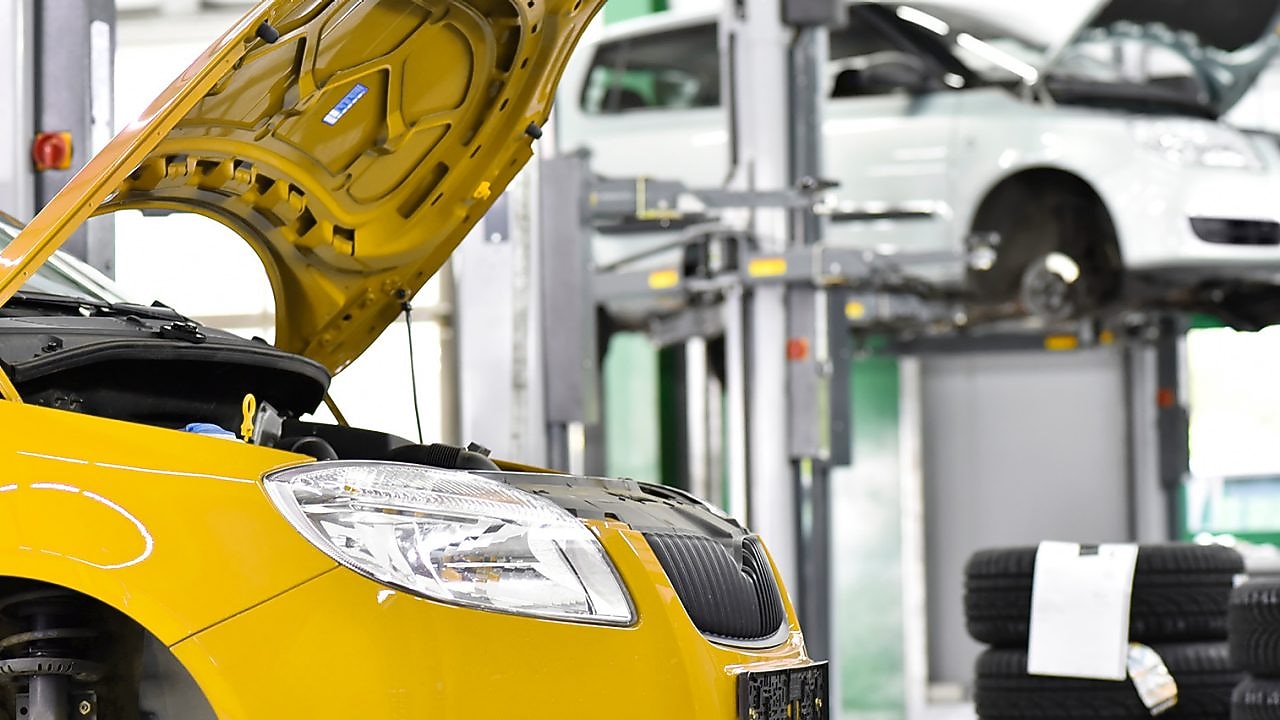 two cars in a garage, one yellow and one white, with their bonnets open, and some car tyres in the background