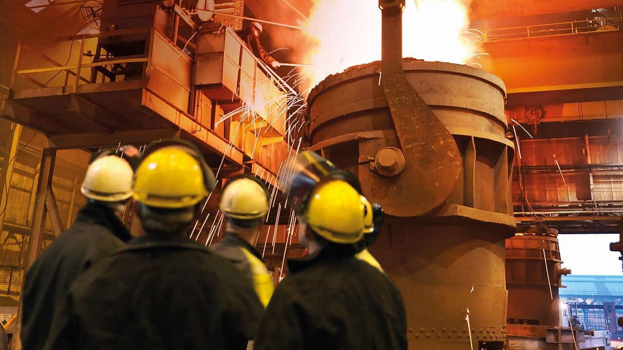 workers watching heavy machinery in a metal processing plant