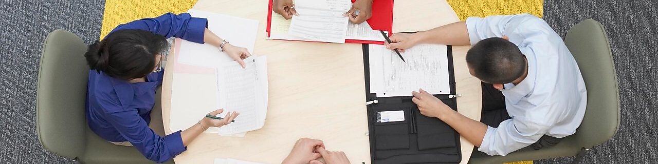 Four business people sitting around a round table reading documents, grey and yellow carpet