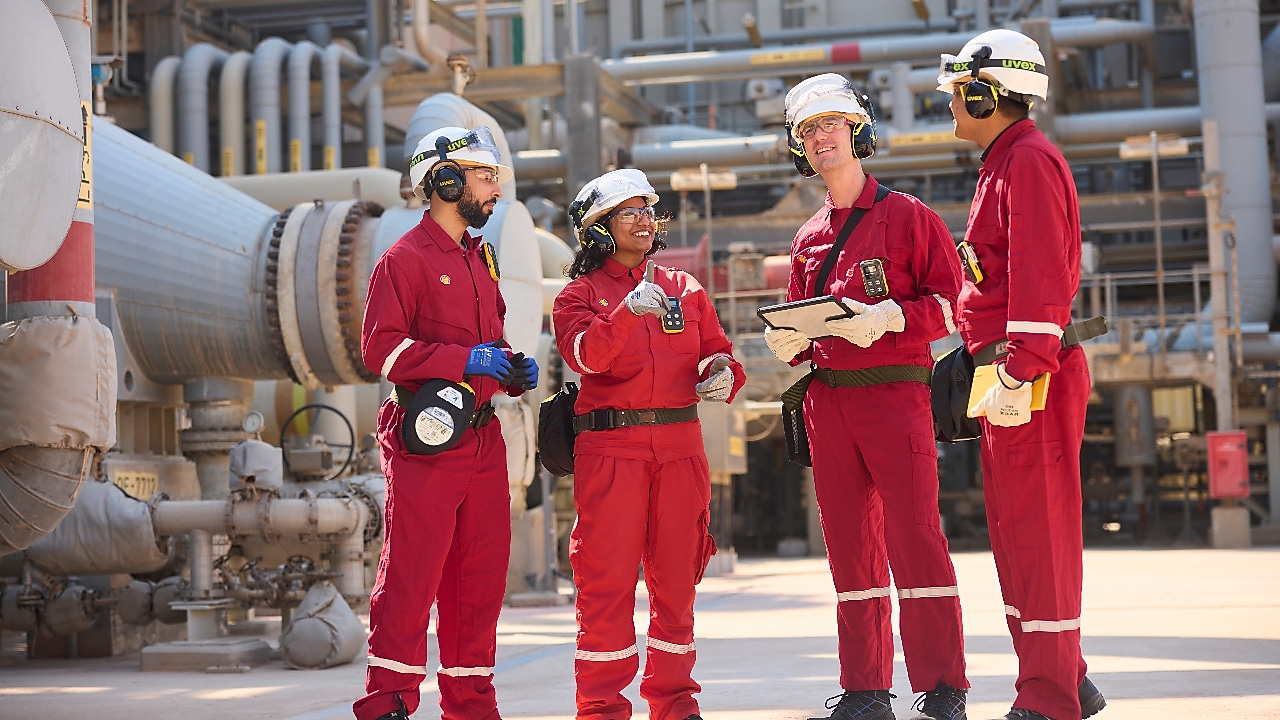 Employees in red PPE and safety gear stand together at the facility, discussing operations and reviewing work and details to ensure safe and efficient operations.