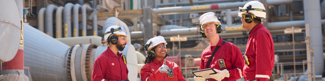 Employees in red PPE and safety gear stand together at the facility, discussing operations and reviewing work and details to ensure safe and efficient operations.
