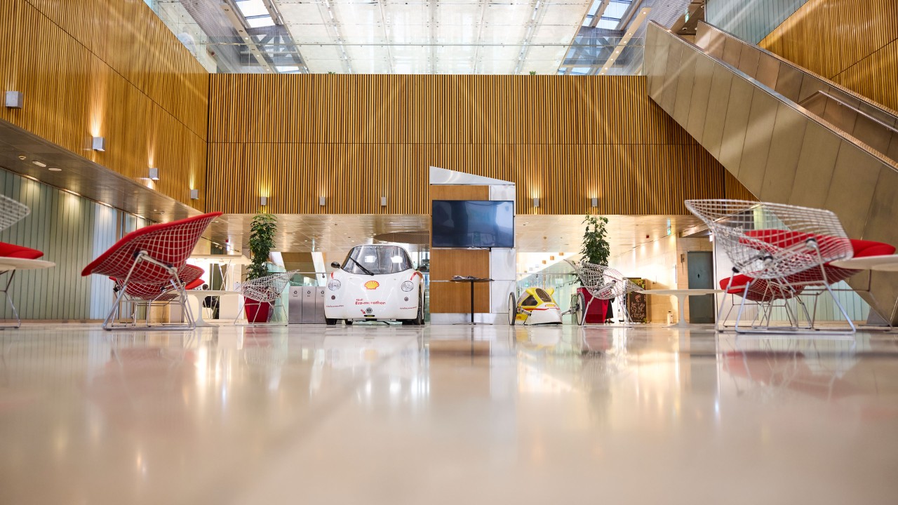 An internal image of the QSRTC lobby featuring experimental solar-powered vehicles, contemporary seating, and a large open atrium with wooden wall panels.