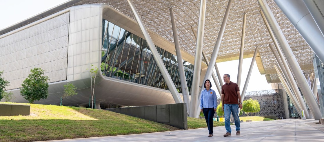 A male and a female walking outside a modern, sustainable building with a large geometric canopy and landscaped grounds.