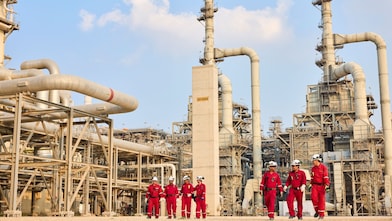 Two groups of production plant employees wearing red safety protective clothing are walking through the production plant.